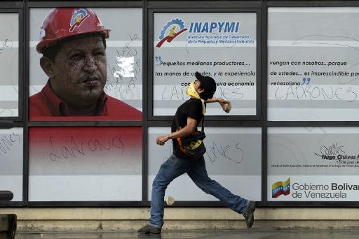 Manifestante opositor atira pedras contra cartaz com foto do ex-presidente Hugo Chávez, em 22 de fevereiro de 2014, em Caracas. Foto: Leo Ramirz/Arquivo/AFP Photo